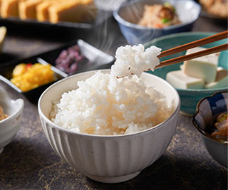 お茶碗に盛られたふっくらとした炊きたての白米を、箸で持ち上げる様子。