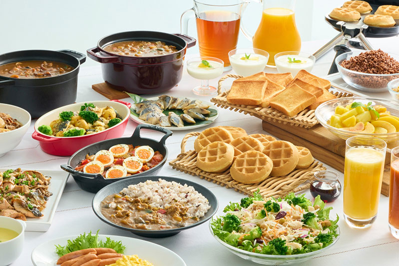 和食と洋食の料理が並ぶビュッフェテーブル。ワッフル、スープ、サラダ、ご飯、味噌汁などが用意されている。