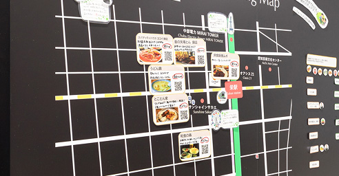 黒い背景の観光マップに、周辺の飲食店情報が写真付きで掲載されている。各店舗のQRコードや料理の画像があり、観光客向けの案内が充実している。