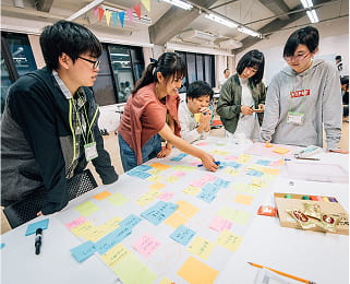 若者たちが付箋を使ってアイデアを整理しながら、チームで議論を進めている。
