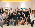 室内で複数名が、笑顔でポーズを取っている。