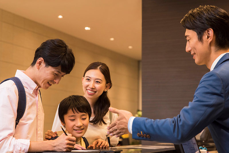 笑顔の家族連れがフロントでスタッフと一緒にチェックインの手続きをしている様子。