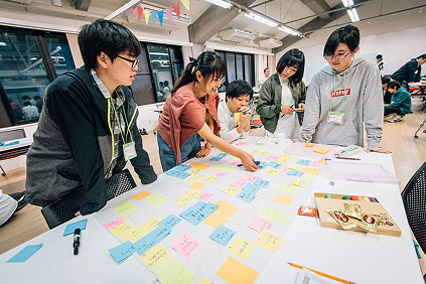 若者たちが付箋を使ってアイデアを整理しながら、チームで議論を進めている。