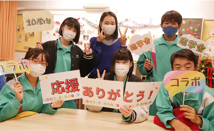 室内で活動する学生グループ。メンバーはマスクを着用し、『応援ありがとう！』と書かれた手作りのメッセージボードを持っている。