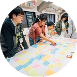 テーブル上の模造紙にカラフルな付箋を貼りながら話し合う学生たちの様子。協働作業の様子がうかがえる。