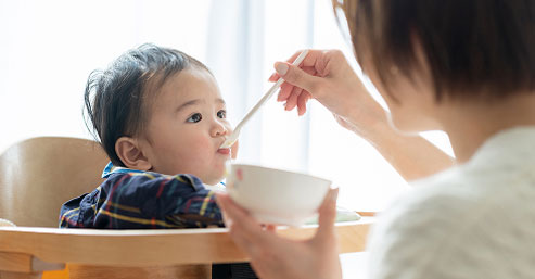 母親が赤ちゃんにスプーンで離乳食を食べさせている様子。